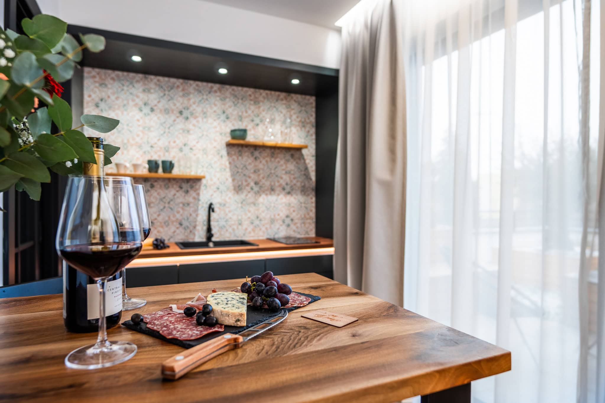 Stůl s červeným vínem a pohoštěním, v pozadí kuchyňský kout apartmánu Španělsko