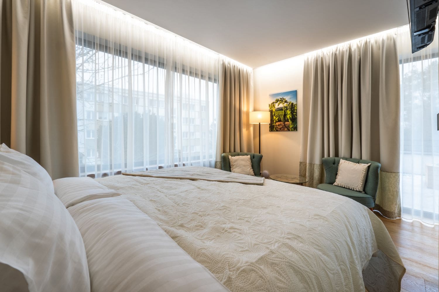 Ložnice apartmánu Itálie s manželskou postelí, béžovými závěsy a zelenými křesly